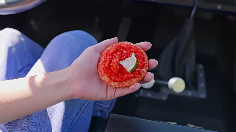 A hand holds a Flamin' Lime Crunch Cookie over bluejean-clad knees while they sit in a car