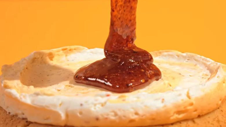 Tajin/mango sauce being poured on a frosted sugar cookie against a yellow background