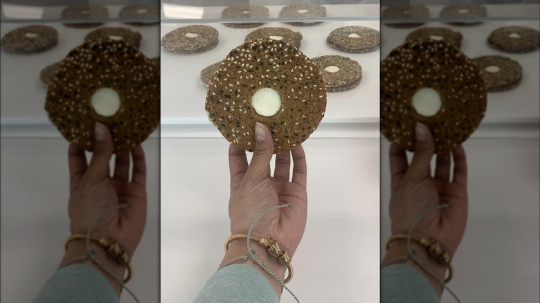 A hand holding an almost everything bagel sandwich cookie from Crumbl in the store.