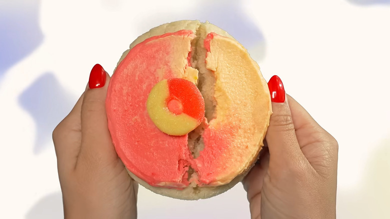 A Peach Ring Cookie from Crumbl being broken in half by two hands