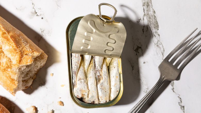 an opened tin of sardines with a fork and baguette