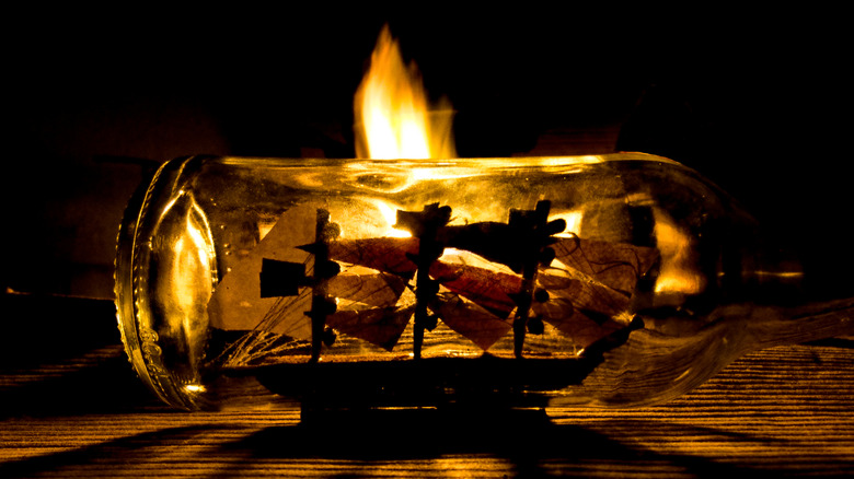 A ship in a bottle is lit by flame from behind