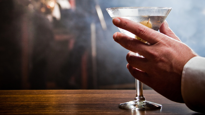 A man's hand holds a martini on a wooden bar