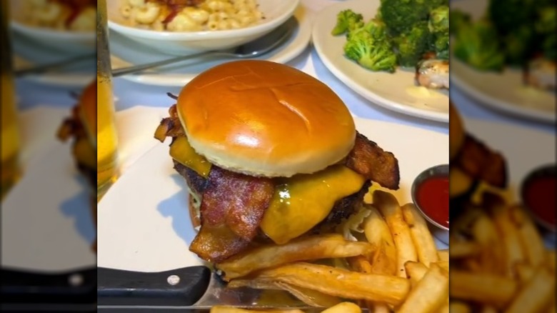 A bacon cheeseburger sitting on a plate with a knife and French fries.
