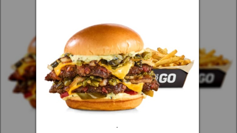 A loaded double cheeseburger sits in front of a tray of fries on a white background.