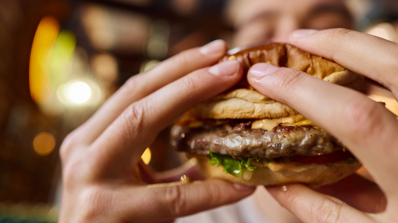 A close up of two hands holding a burger with the person blurred in the background.
