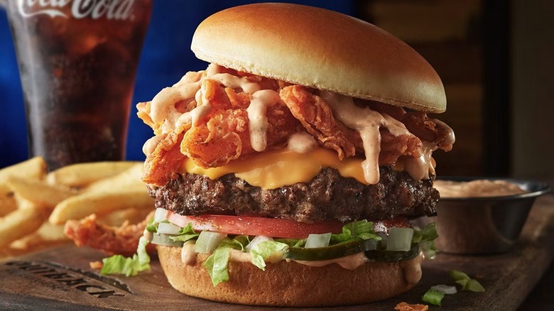 The Bloomin' Burger sitting on a cutting board with fries and a glass of soda in the background.