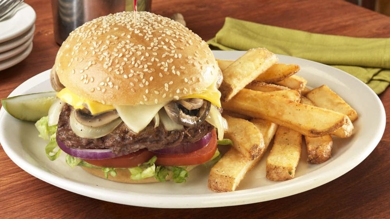A loaded cheeseburger sitting on a plate with steak fries on a wooden table.
