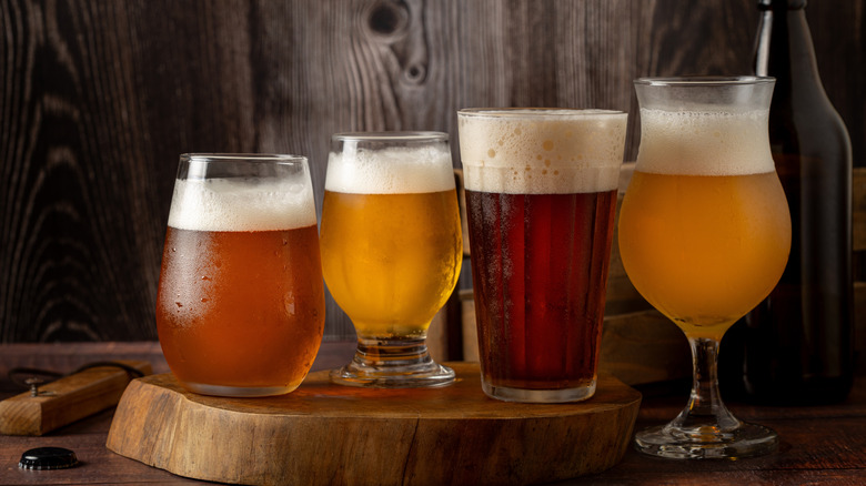 A line of craft beers on a wooden table in variously-shaped glasses