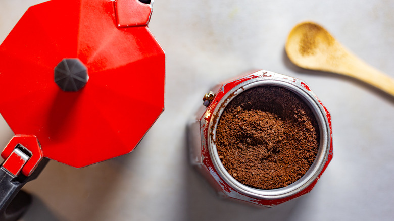 Top-down view of a red moka pot; the lid is off to the side, the body is full of coffee grounds