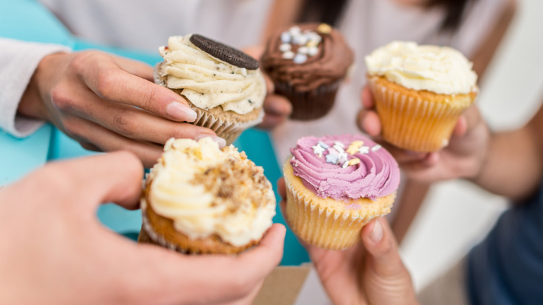 Five hands holding cupcakes of various flavors
