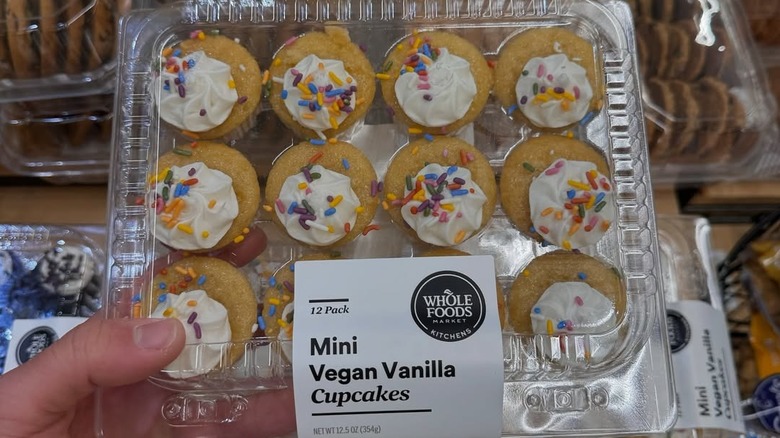 Hand holding plastic package with one dozen mini vegan vanilla cupcakes