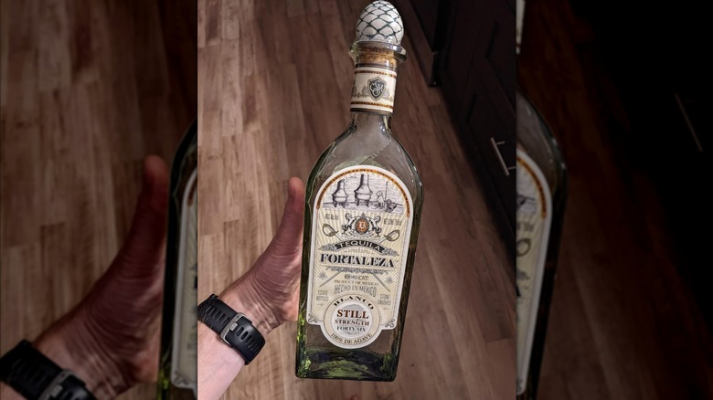 A PoV shot of an unopened bottle of Fortaleza Still Strength in a person's hand