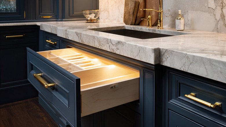 A kitchen interior featuring a marble countertop and dark blue cabinets with golden handles and a drawer open