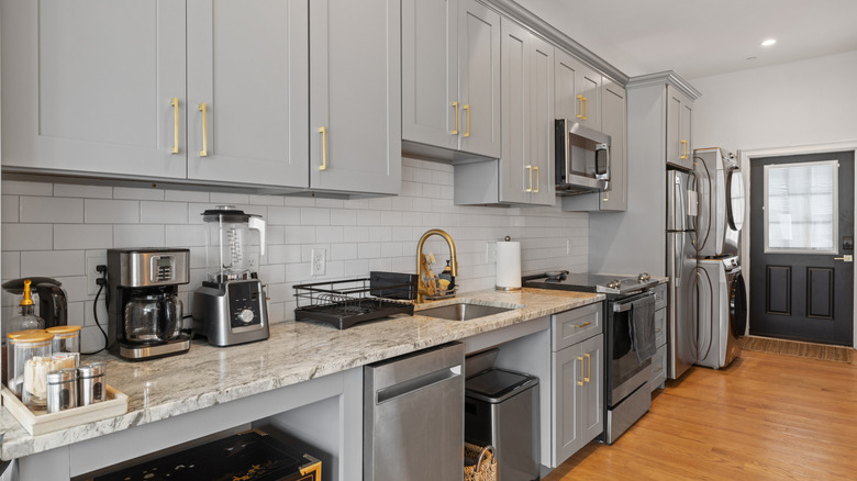 grey kitchen with gold hardware on door cabinets and black and silver appliances