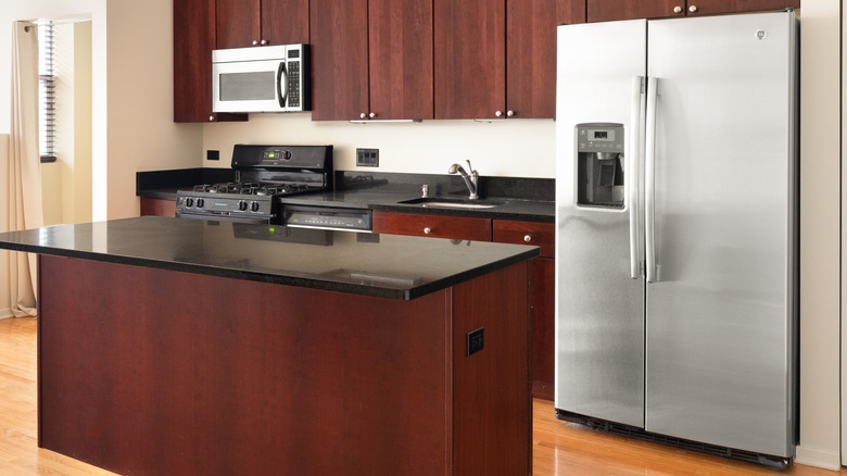 A bright kitchen with cherry cabinets, stainless steel GE appliances, black granite countertops, and hardwood floors