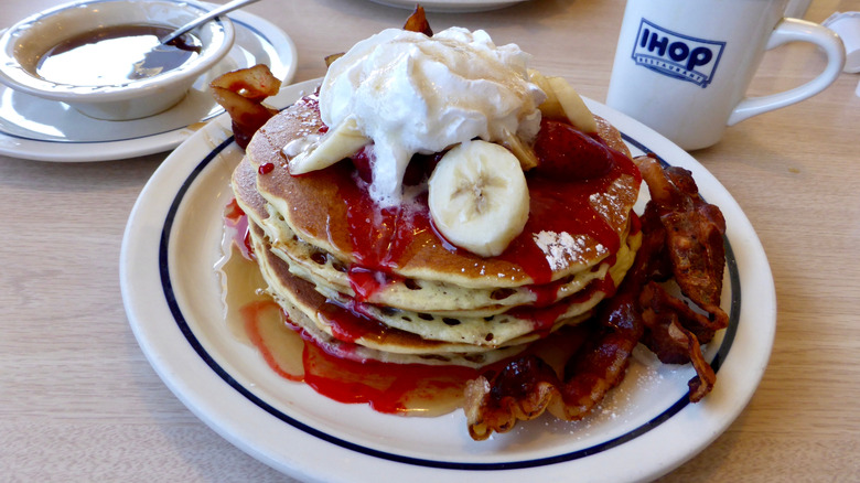 IHOP pancake stack with syrup, bananas, whipped cream, and bacon on the side next to cup