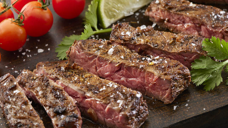 Slices of steak with tomatos on a wooden board