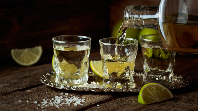 Pouring tequila into shot glasses with limes and salt