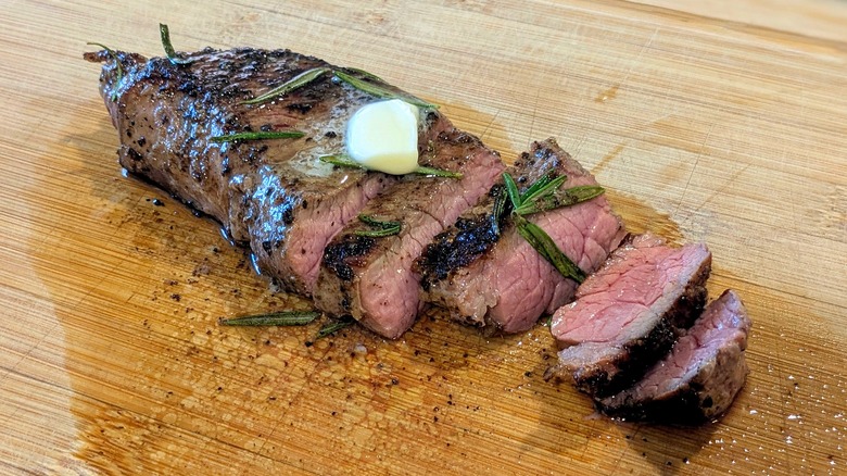A small steak, partially sliced, with rosemary and butter on a cutting board