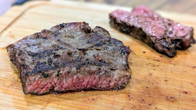 A close-up of the pink midsection of a skirt steak with a charred exterior on a cutting board