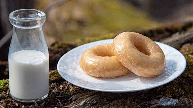 Plate with two glazed donuts and glass of milk on log