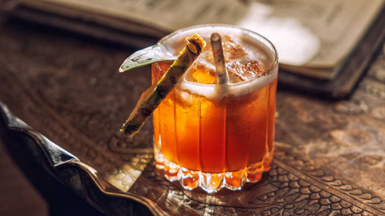 A rum old fashioned garnished with pineapple on an ornate wooden surface