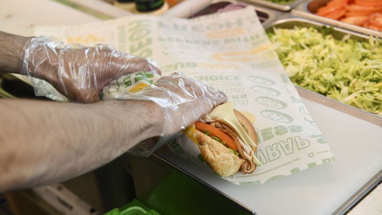 Gloved hands wrapping a Subway sandwich