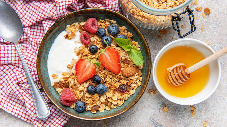 Overhead shot of yogurt bowl topped with granola and fresh fruits, alongside honey, napkin, and spoon