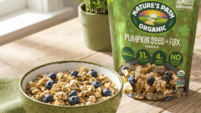 Bowl of Nature's Path Organic Pumpkin Seed + Flax granola alongside bag, napkin, and plant on table