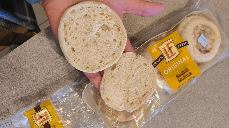 Hand holding cut open English muffin over Aldi packet on countertop