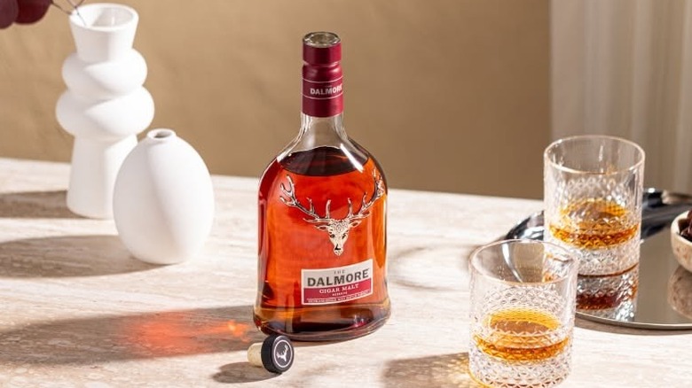 A bottle of Dalmore Cigar Malt Reserve on a brightly lit table next to two filled glasses