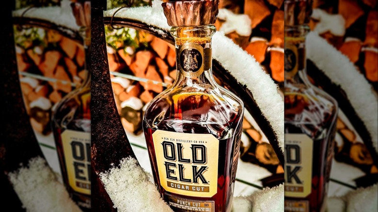 A bottle of Old Elk Cigar Cut posed on a snow-covered metal railing