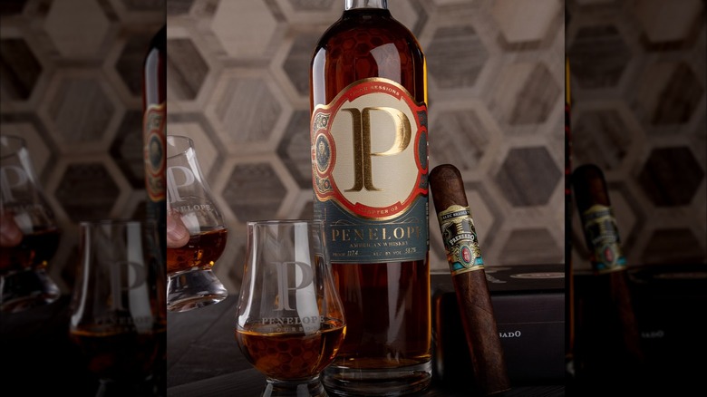 A bottle of Penelope Cigar Sessions: Chapter 2 with a branded cigar and glass either side