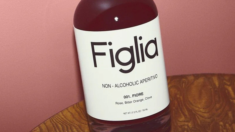 Close-up of Figlia Fiore bottle on wood table against pink background.