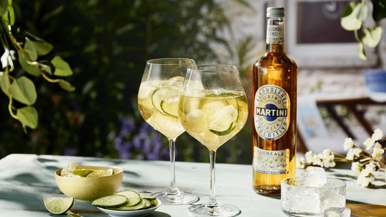 Two spritz mocktails alongside a Martini Floreale bottle and lime and cucumber wedges