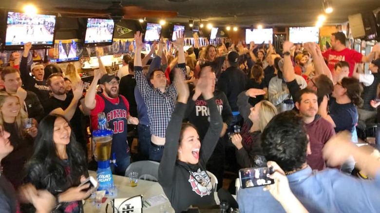 Packed room of people cheering with sports on the televisions