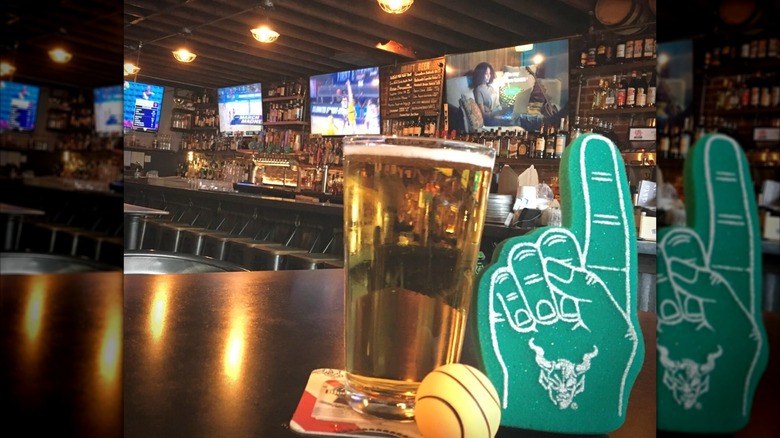 Foam finger and beer on table with bar and TVs in background