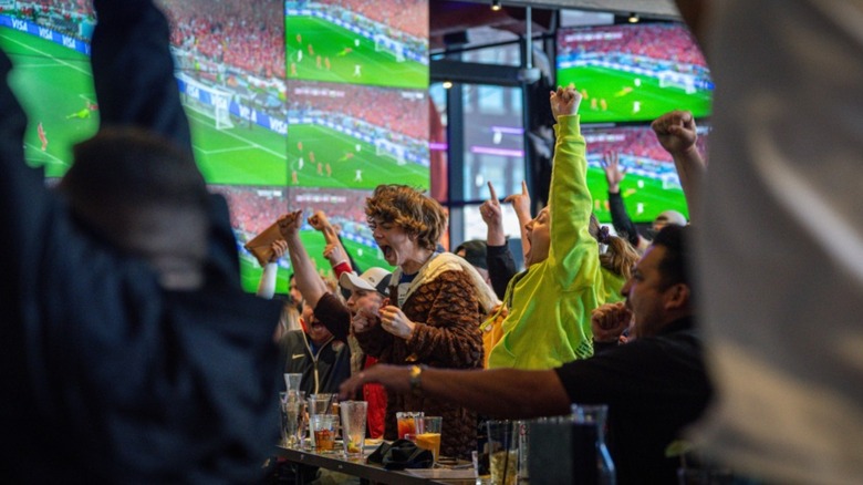 Screaming sports fans at the bar with television wall in the background