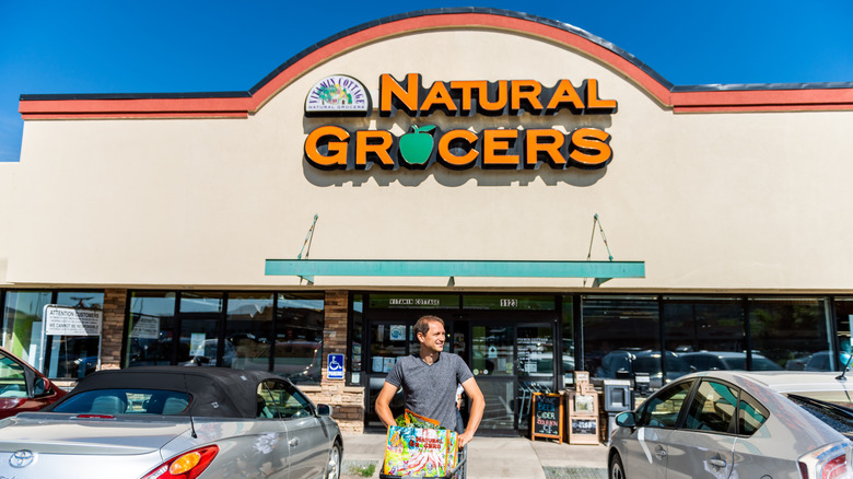 Man pushing shopping cart in parking lot of Natural Grocers