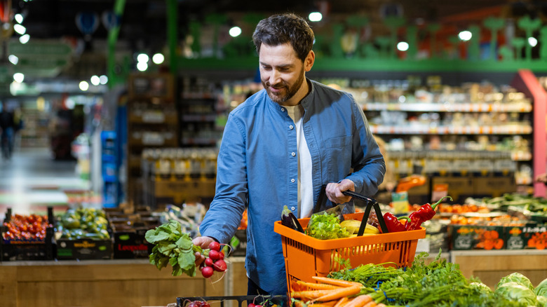 Man adding vegetables to grocery basket in dimly lit store