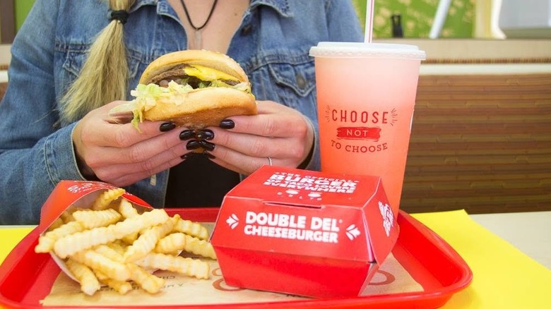 Hands holding a Double Del Cheeseburger with fries and drinks on tray