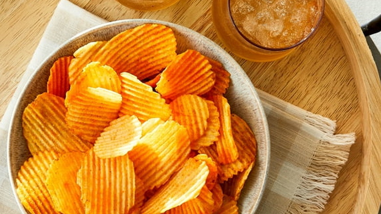 Bowl of rippled cheddar and sour cream flavored chips and a drink