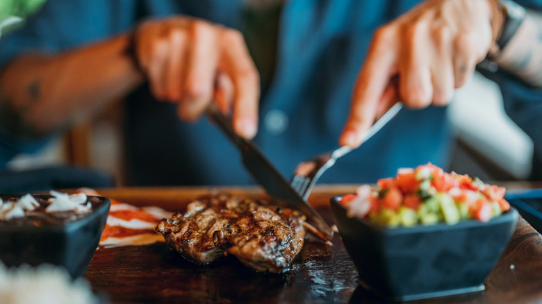 Hands slicing into steak with a fork and knife in a restaurant