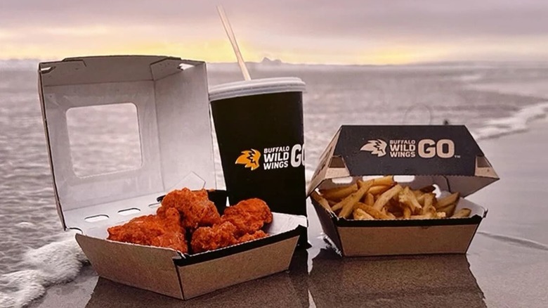 Boneless wings and fries in takeout containers on beach with a soda