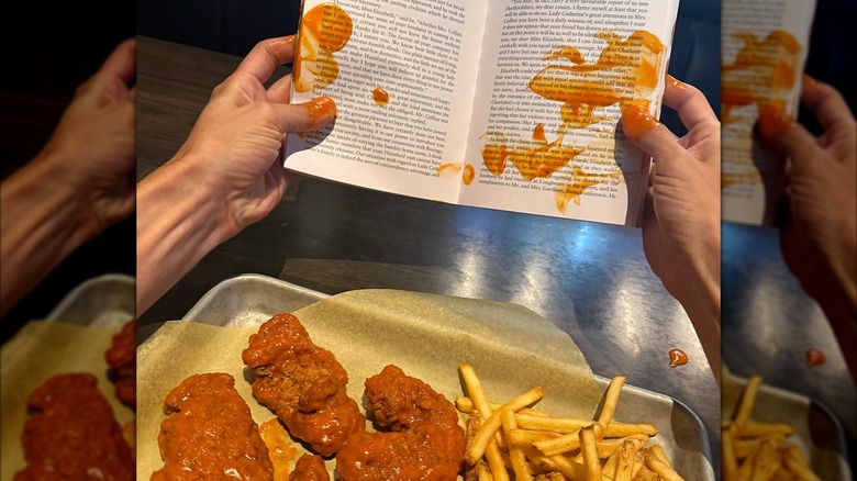 Tray of boneless wings and fries with person holding a sauce-covered book