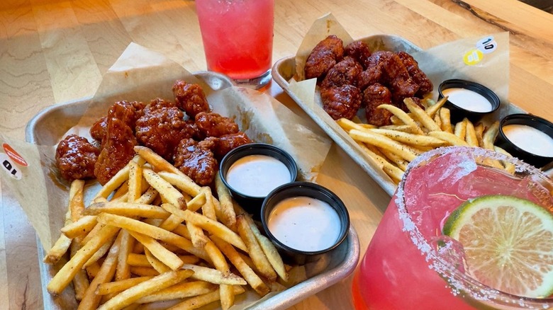 Trays with wings, fries, and dipping sauces and cocktails on table