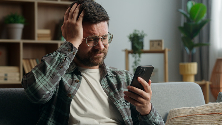 Frustrated guy in living room looking at smartphone