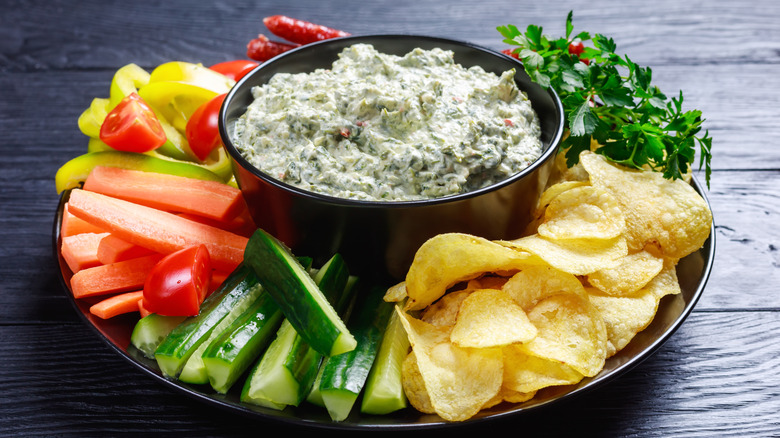 Cold spinach dip in bowl surrounded by crudite and chips