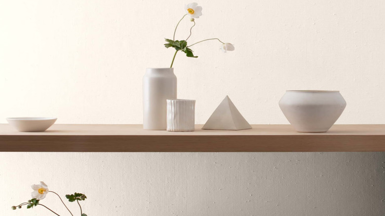 Wooden surface holding white dishes and flour vase against white wall